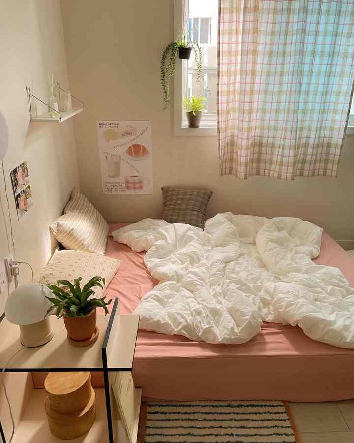 柔らかいナチュラルトーンの寝室、ピンクのマットレスと白い掛け布団、様々な柄の枕が調和する居心地の良い空間