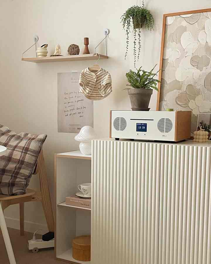 ベージュとホワイトのトーンでまとめられたシンプルなリビング、木製家具と植物、ベビー服のオブジェが温かみのある雰囲気を演出しているインテリア