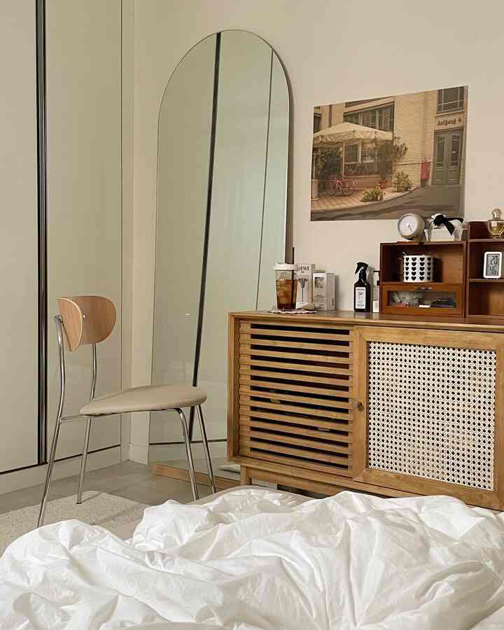 ナチュラルな木目調と白を基調とした寝室、木製収納キャビネットと全身鏡が配置された雰囲気のある空間