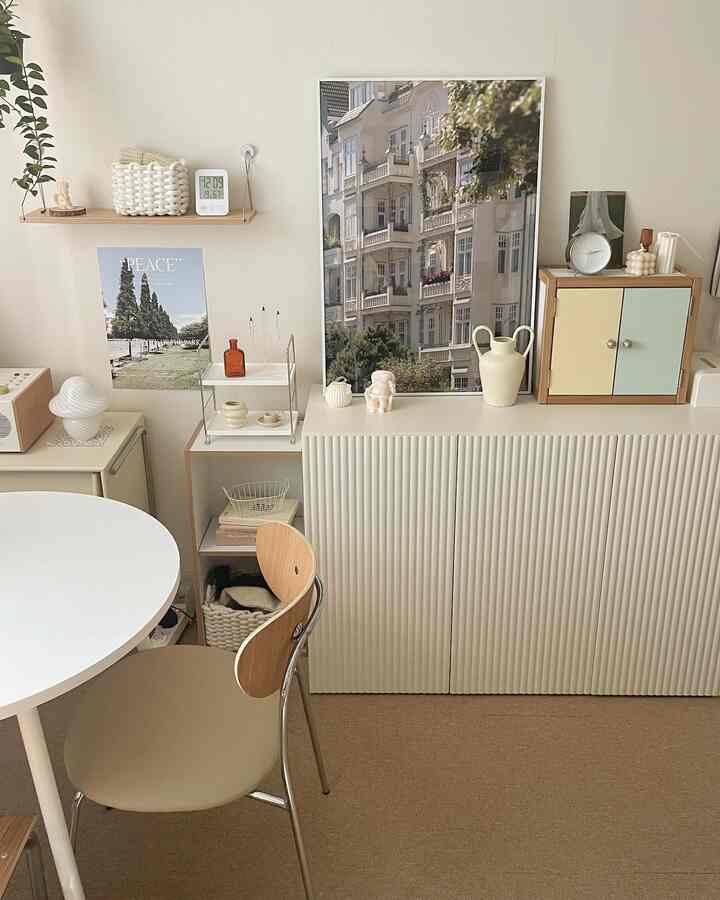 ナチュラルトーンのリビングとダイニングルーム、クリーム色の収納キャビネットと丸い白いダイニングテーブル、木製のダイニングチェアが配置された清潔で居心地の良いインテリア