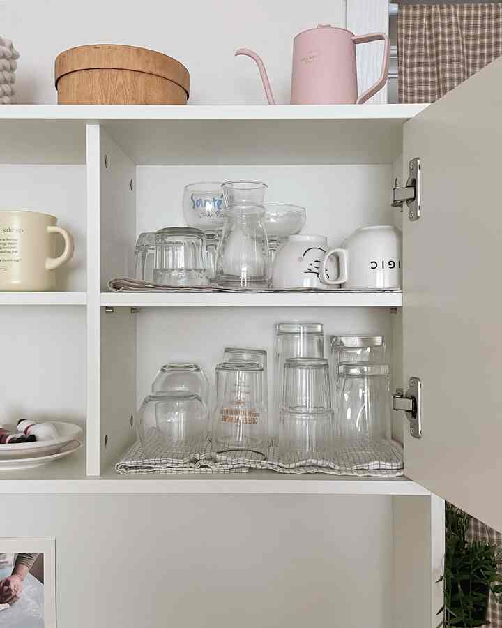 明るいホワイトトーンのキッチン収納棚に、整然と並べられたグラスやマグカップ、ピンクのドリップケトルが配置された自然で清潔感のある空間