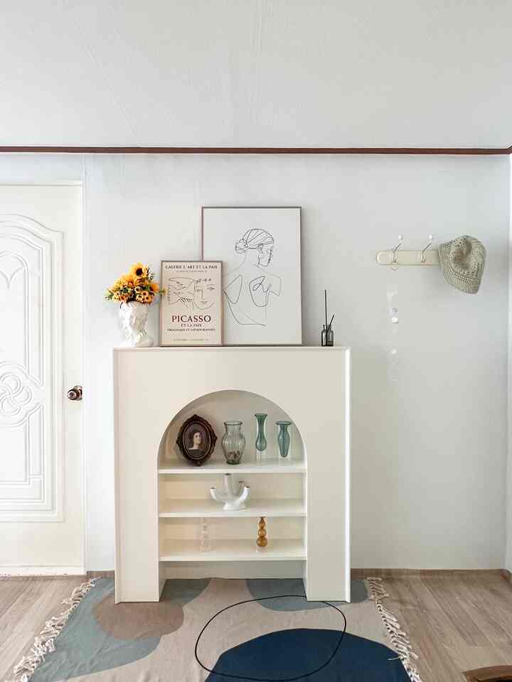 アイボリー色のアーチ型シェルフにヴィンテージのオブジェや額縁が配された白い壁の玄関スペース