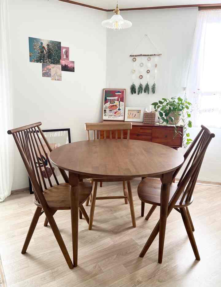 温かみのある木目調と白を基調とした4人用ダイニングルーム、丸い木製のダイニングテーブルと椅子4脚、ポスターとペンダントライトが配されたナチュラルでヴィンテージ感のあるインテリア