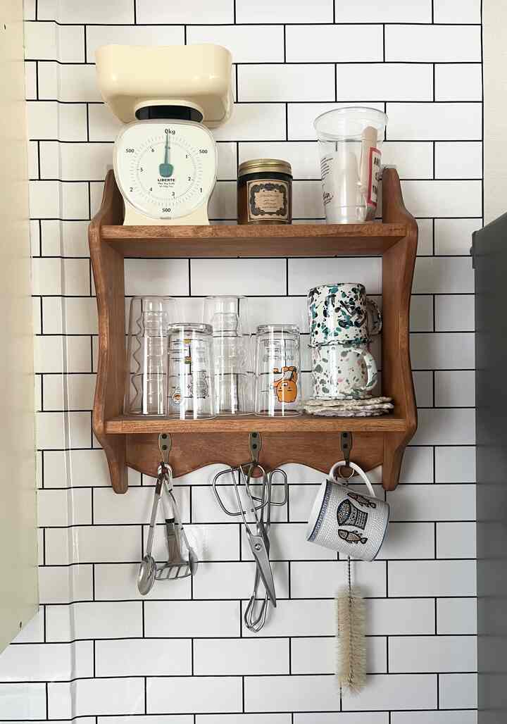 白いタイルの壁を背景に、茶色の木製棚にキッチン用カップと調理器具が配置された雰囲気のあるおうちカフェ空間