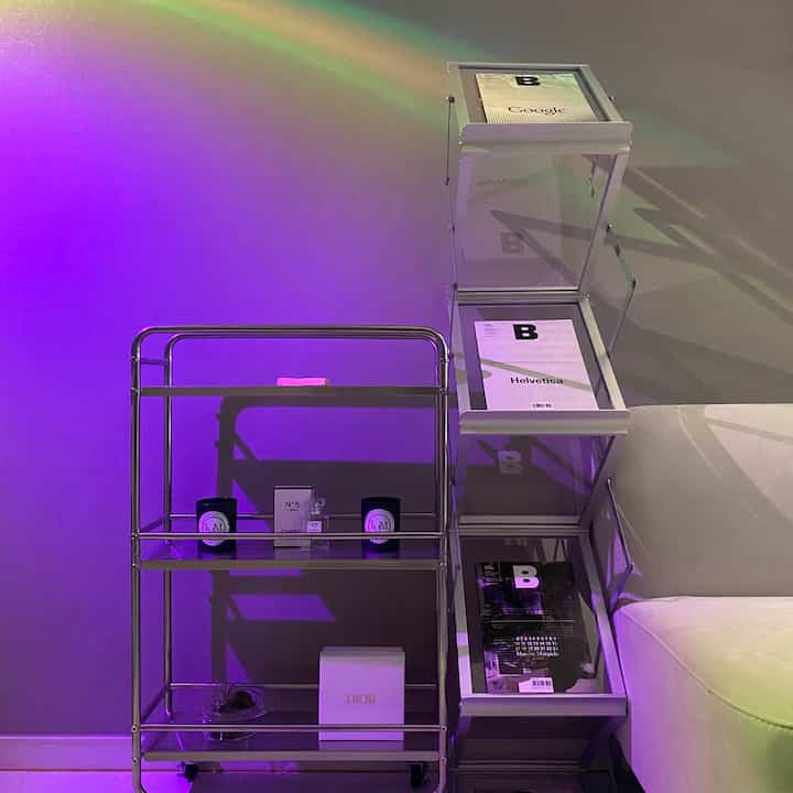 モノトーンとシルバーのリビングスペースの一角、サンセットのアクセント照明がトロリー、マガジンラック、ソファを包む雰囲気あるインテリア