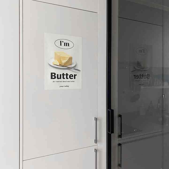 モノトーンでミニマルなキッチン、白いキャビネットとバターポスターが配置された印象的な空間