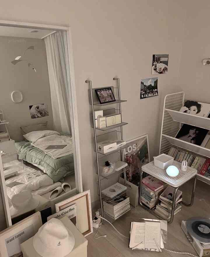 白とグレーのトーンの寝室、金属製の棚と本棚、多くの本が積まれており、落ち着いたミッドセンチュリーモダンの雰囲気のあるインテリア