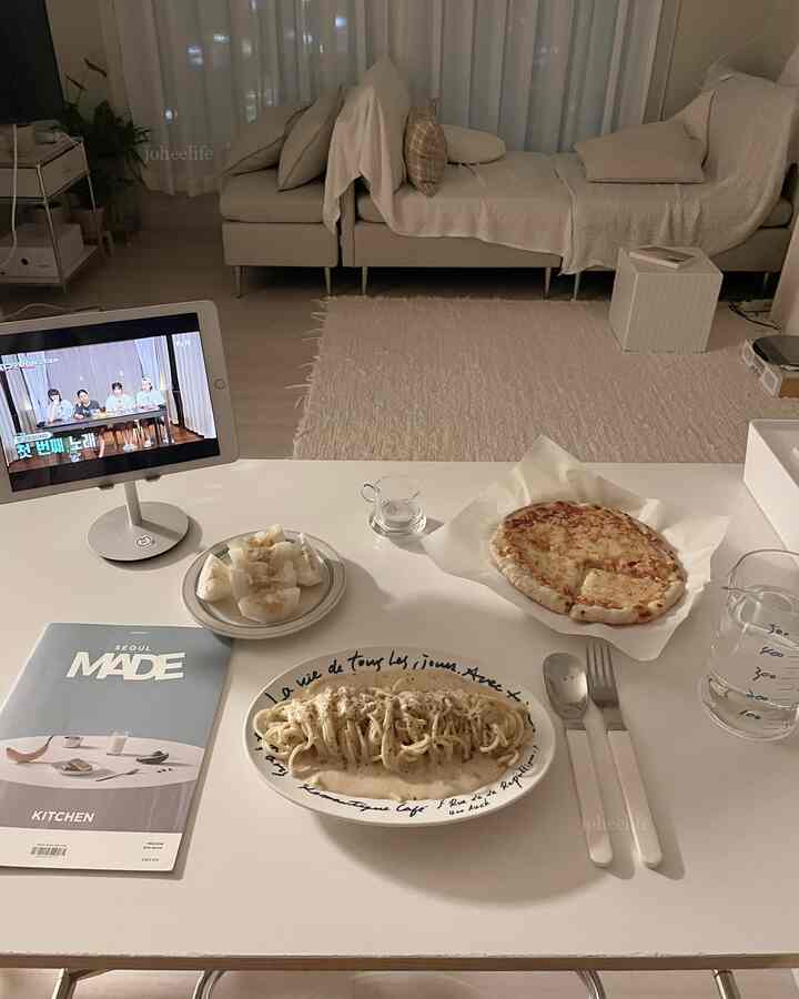 温かみのあるアイボリーとホワイトのトーンのリビング、シンプルなソファとラグ、ダイニングテーブルにホームカフェスタイルの食事が置かれた落ち着いた空間