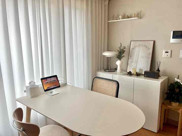 白とナチュラルトーンのリビング、シンプルなダイニングテーブルと椅子、カーテン、照明、額縁が配置された雰囲気のあるインテリア