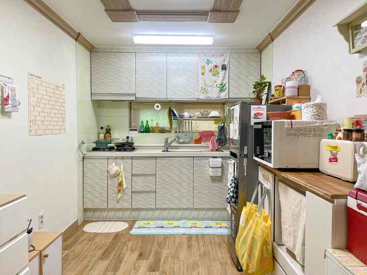 白と茶色の調和が取れた小さなキッチン、ファブリック小物や収納家具が配置された雰囲気のあるインテリア