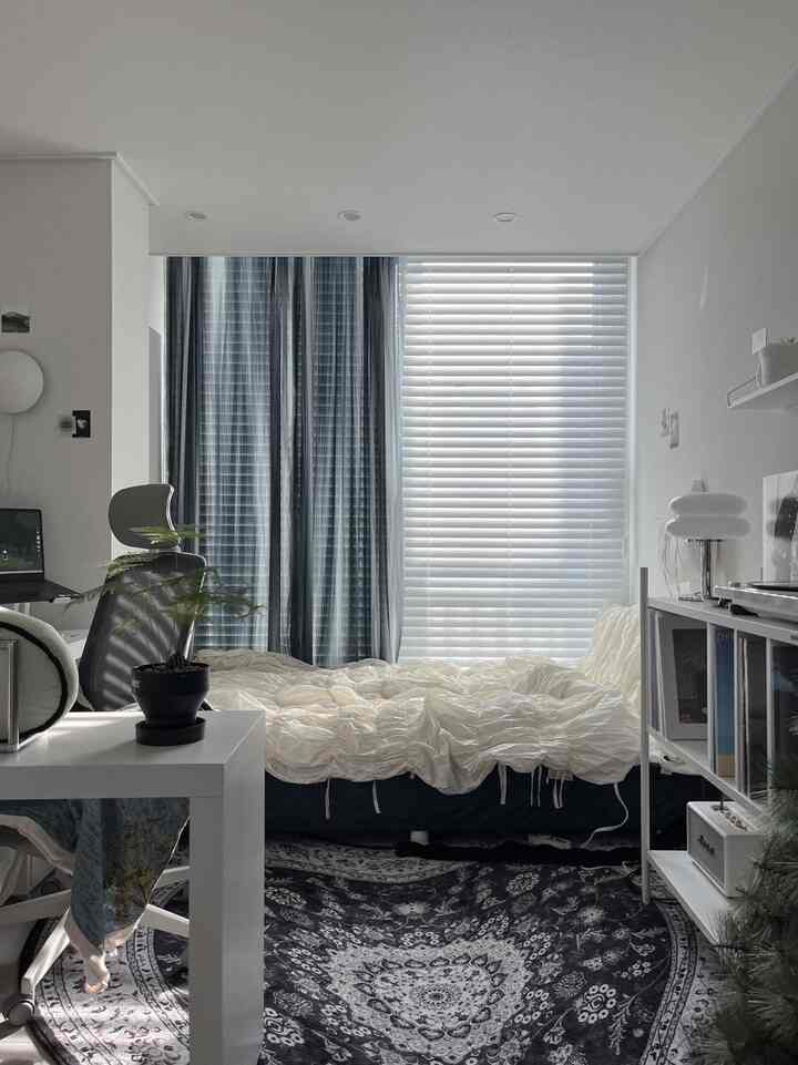 白とネイビーの色調の寝室、中央にベッドとアイボリーのギャザリング掛け布団カバー、左側にはデスクとオフィスチェアが配置された落ち着いた空間