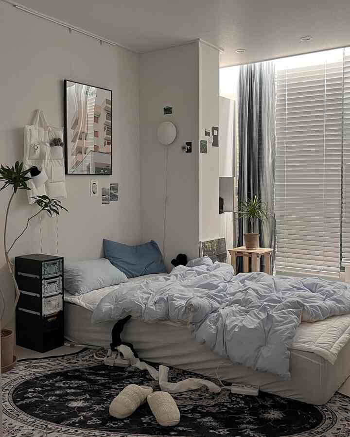 淡い青の寝具と木目調のアクセントがある柱付きの狭い寝室のインテリア