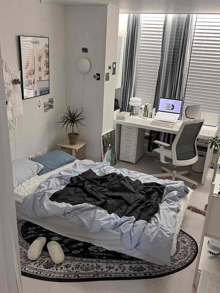 白と青のトーンのワンルーム寝室、ベッドとデスク、オフィスチェアが配置されたコンパクトな在宅勤務スペース