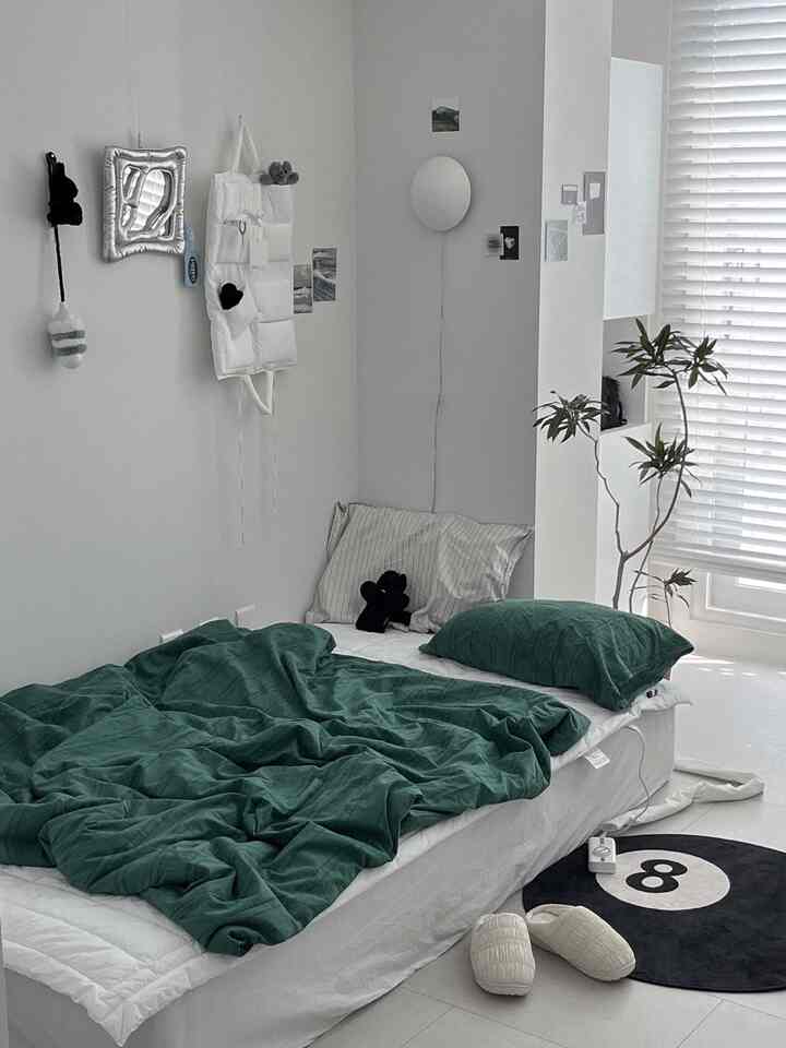 白い壁と床に囲まれ、緑の寝具が印象的な寝室、シンプルで落ち着いた雰囲気のインテリア