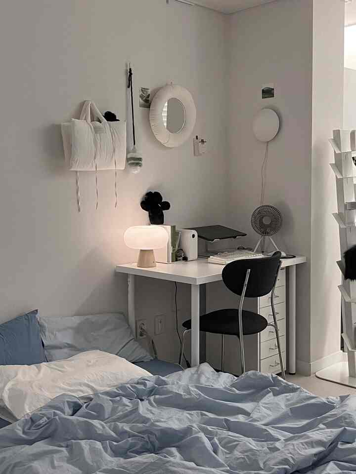 白い壁と青い寝具のコンパクトな寝室、すっきりとしたデスクと照明が配置された雰囲気のあるワークスペース