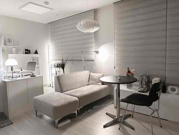 白とグレーのトーンのリビングルーム、ソファと丸テーブル、ペンダントライトとテーブルランプが配置された落ち着いたカフェ風インテリア