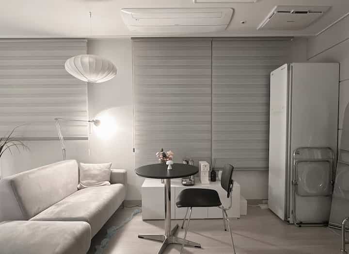 白を基調としたリビングとキッチンの空間、シンプルなソファとラウンドテーブルが配置された清潔感のあるミニマルなインテリア