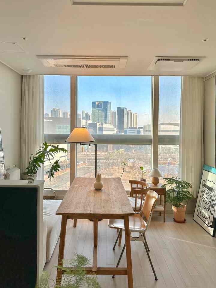 ナチュラルな木目調のワンルームダイニング、広いダイニングテーブルとフロアランプ、カーテンと植物が配置された雰囲気のあるインテリア