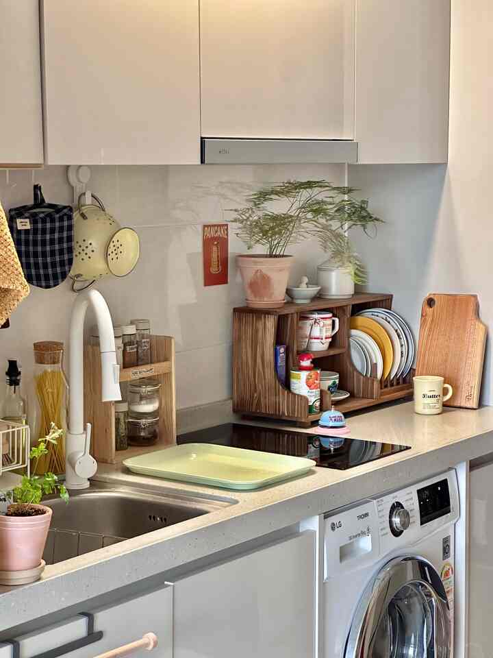明るくナチュラルな色調のキッチン、木目調の食器収納と白い蛇口、植物が配置されたすっきりとした雰囲気のインテリア