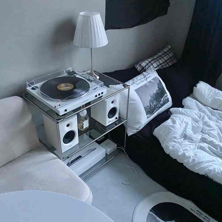モノトーンの黒と白が調和するワンルームの寝室、ソファベッドに枕、棚の上にはターンテーブルとスピーカーが配置されたシンプルでモダンなインテリア