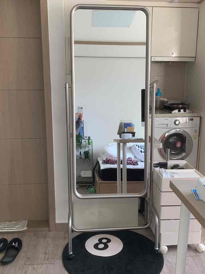 シルバーフレームのミッドセンチュリーモダン全身鏡が置かれた黒いラグの小さなワンルームリビングスペース