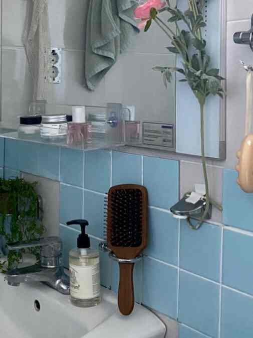 淡い青のタイルと白い洗面台があるバスルーム、鏡とタオル掛け、植物が配置された雰囲気のある空間