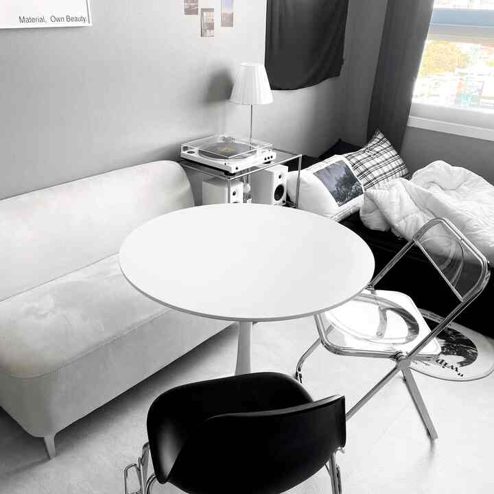 モノトーンのワンルームリビング、丸テーブルと多様な椅子、ソファが配置されたモダンなインテリア