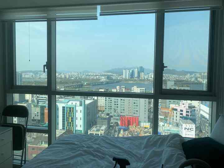 白を基調とした寝室、大きな窓にブラインドと金属製ベッドフレームが配置されたミニマルで落ち着いたインテリア