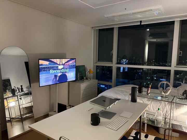 白と木目調の調和がとれたワンルームの寝室兼ホームオフィス空間、大きな窓から夜景が見えるシンプルなインテリア