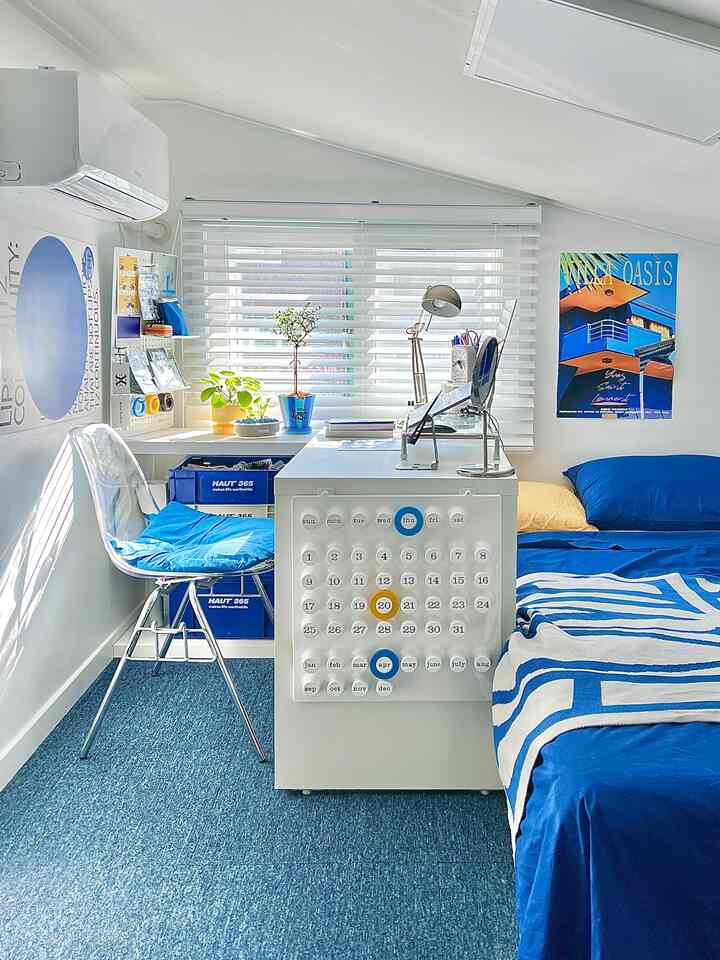 明るいホワイトとブルーのトーンの寝室、デスクと窓のブラインド、ブルーポスターが配置された快適な一人暮らしの空間