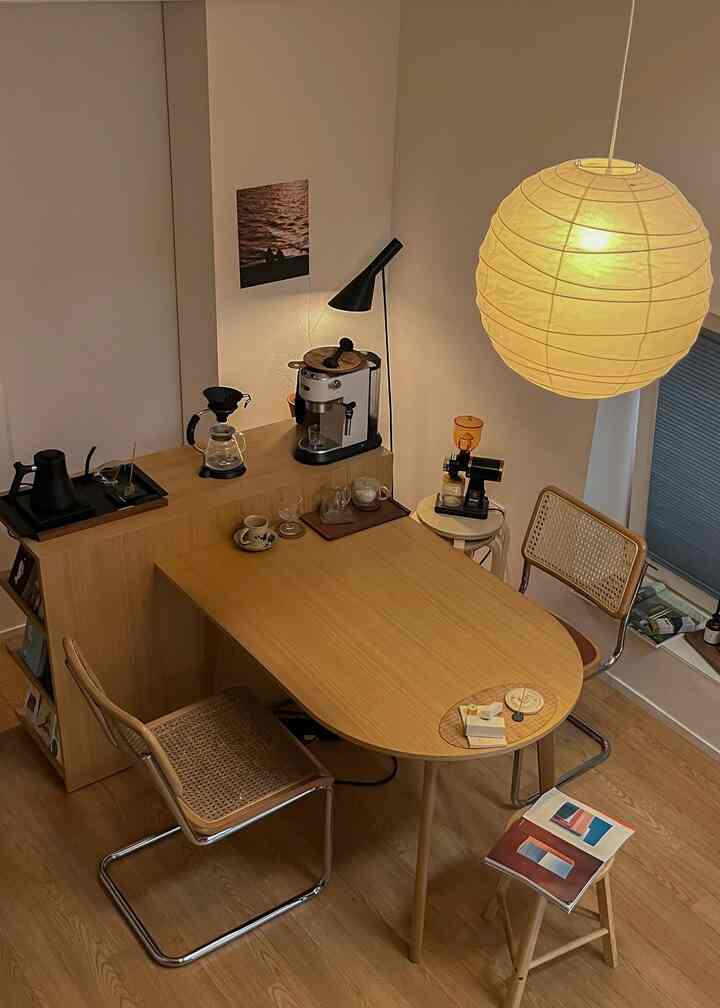 ナチュラルな木目調のコンパクトなホームカフェ、半円形テーブルとラタンチェア、コーヒーマシンが配置された雰囲気のあるインテリア