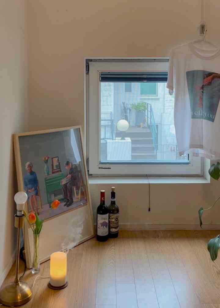 ナチュラルカラーの木目調フローリングと額縁、ディフューザーが置かれた小さな窓辺の雰囲気あるコーナー