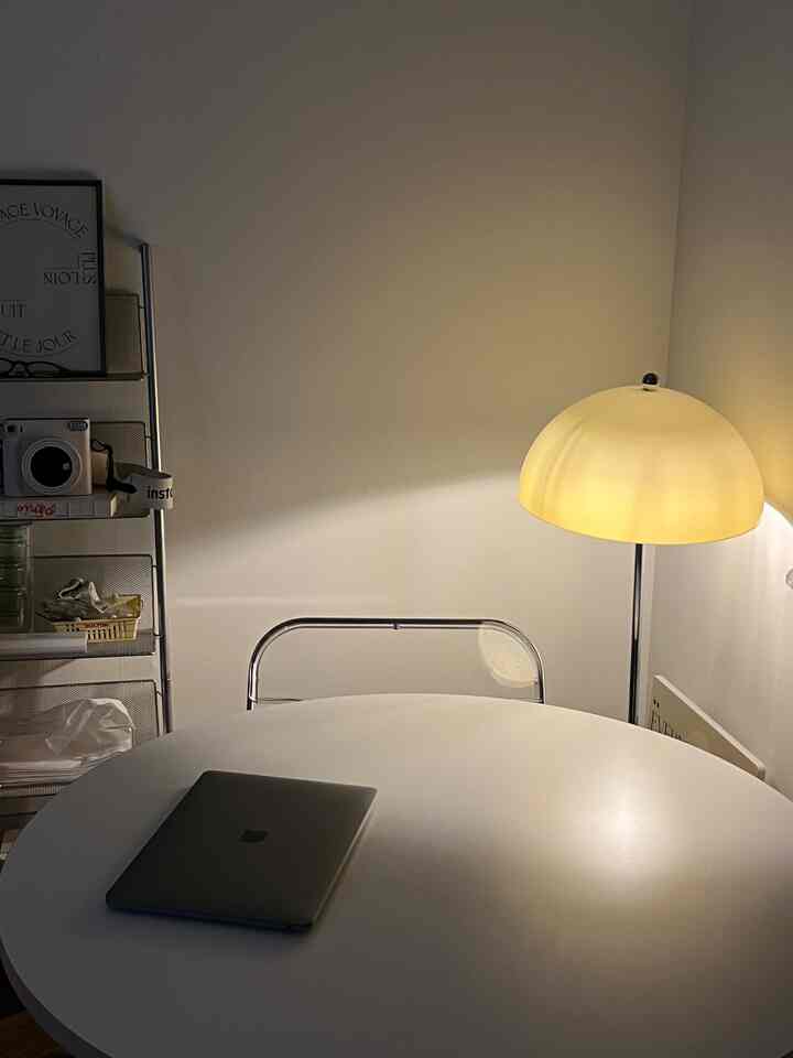 暖かい黄色の照明がある白いワンルーム、丸テーブルとメタルチェアが配置されたシンプルな作業空間