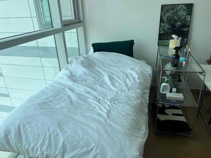 白を基調とした寝室、白い布団と黒い枕が置かれたベッドと右側に配置されたモダンなナイトテーブルが印象的な空間