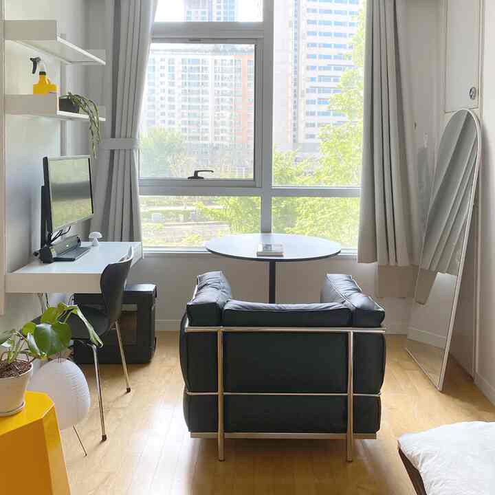 ホワイトとブラックのトーンが特徴のコンパクトな一人暮らし向けホームオフィス空間、ブラックのソファと丸テーブルが配置された明るく清潔な部屋