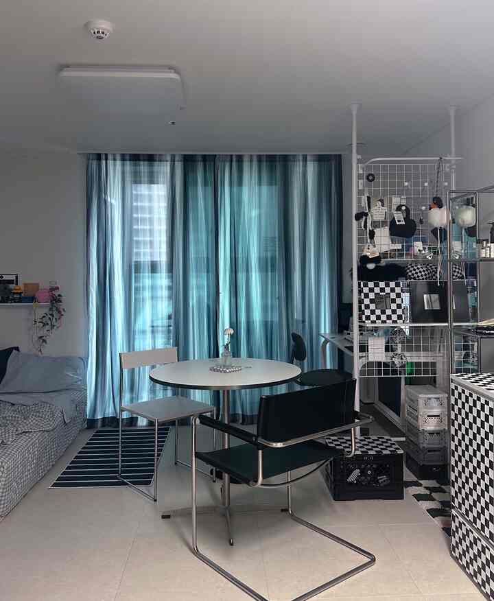 清涼感のあるモノトーンのリビング、中央に配置された丸いダイニングテーブルと黒いアームチェアが特徴的なモダンなインテリア