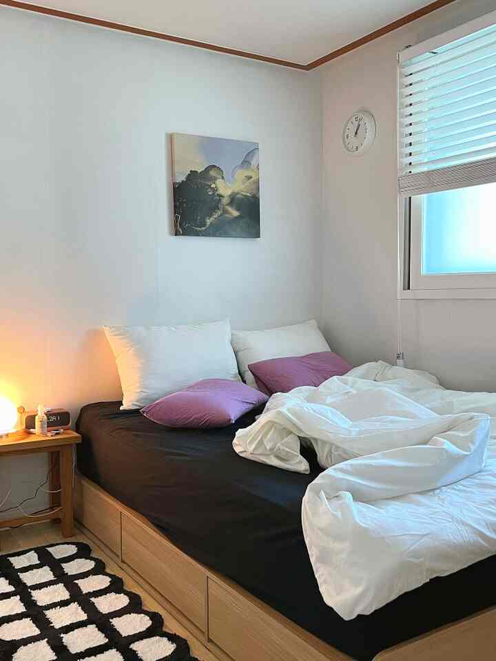 ホワイトと木目調が調和した寝室、ブラックのベッドシーツとパープルのクッションがアクセントの居心地の良い空間