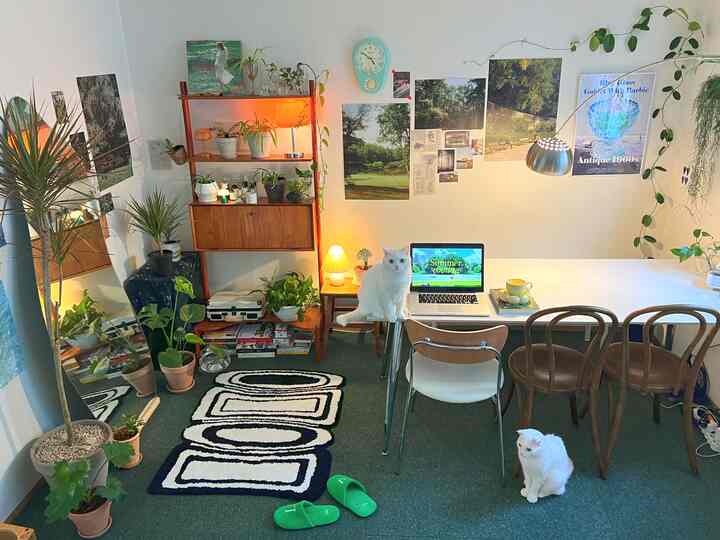 グリーンのカーペットとミッドセンチュリーモダンスタイルのダイニングテーブル、豊富な植物と二匹の白い猫がいるナチュラルなリビングルーム