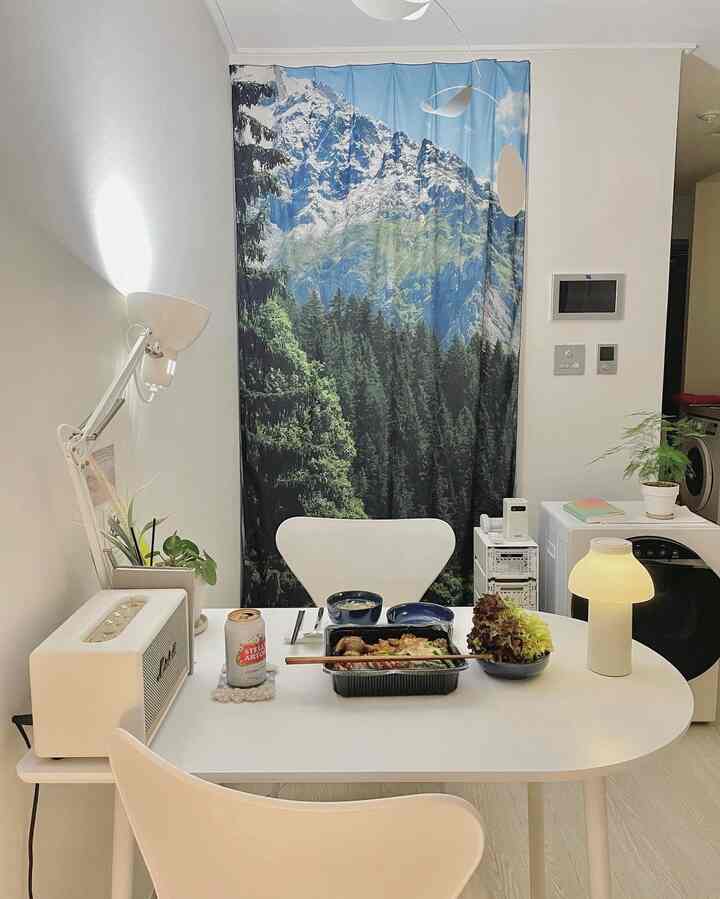 白と緑のトーンのダイニングルーム、ダイニングテーブルと椅子、山の景色のファブリックポスターが配置された雰囲気のあるインテリア