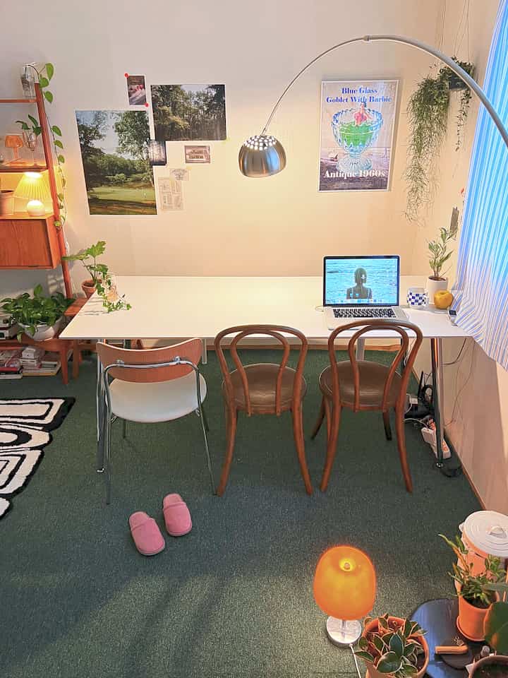 ディープグリーンのカーペットが敷かれたカフェ風のホームオフィス空間、白いダイニングテーブルと木製椅子、シルバーのアーチ型フロアランプが配置された雰囲気のあるインテリア