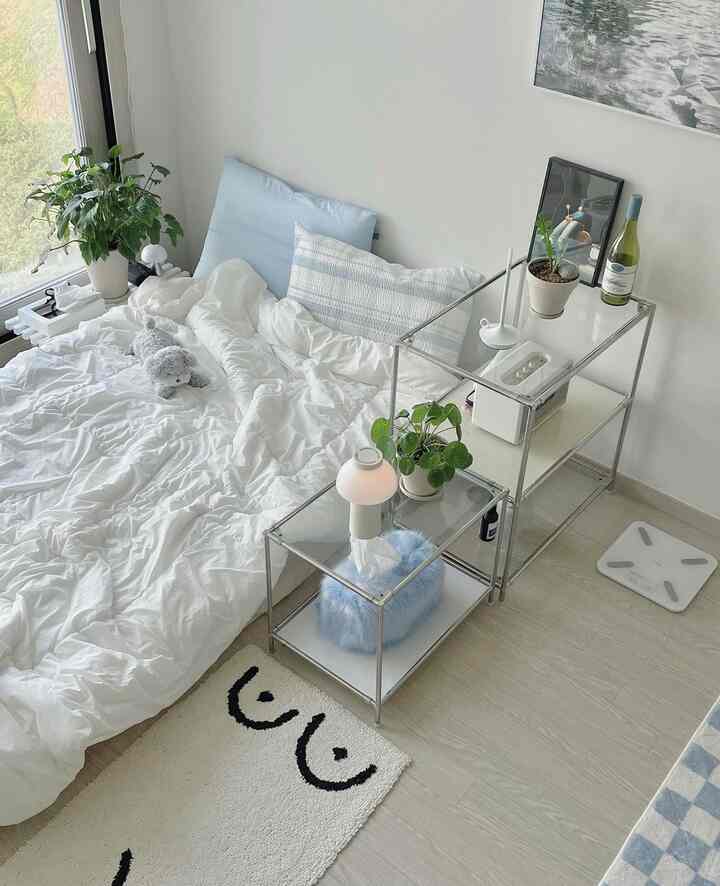 白とスカイブルーのトーンが印象的な寝室、ナチュラルでミニマルなインテリアにテーブルランプとシェルフが配置された空間