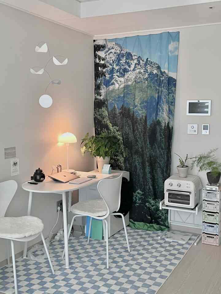 ホワイトとブルーのトーンが特徴のコンパクトなリビングルーム、テーブルランプと植物が配置された清潔感のあるホームオフィスインテリア