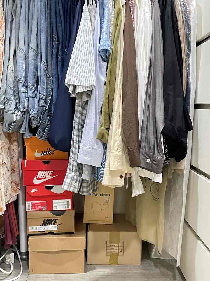 白と黒の服と積み重ねられた靴箱がある狭い部屋の収納スペース