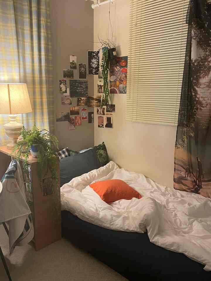 ホワイトとネイビーの色調のコンパクトな寝室、オレンジの枕とフロアランプが配置された雰囲気のある空間