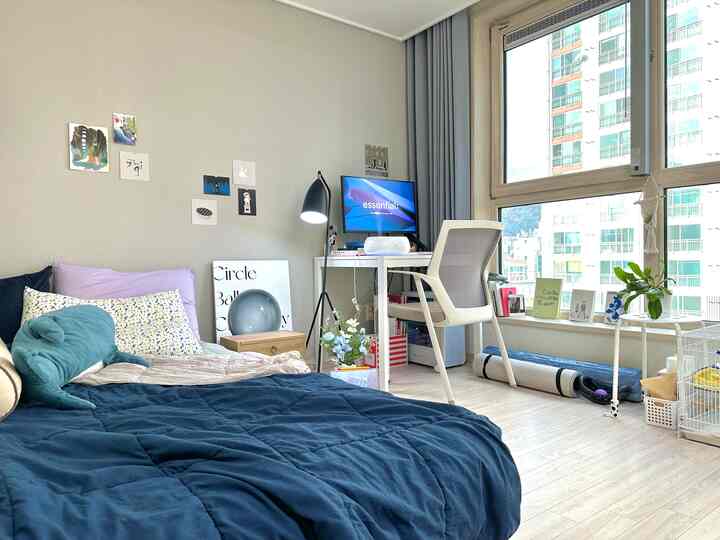 白と青のトーンのコンパクトな寝室、窓辺にデスクとチェアが配置されたシンプルで自然なモダンなインテリア