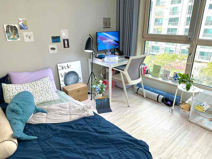 白とネイビーを基調としたワンルームのホームオフィス兼寝室空間、自然光とすっきりしたインテリアが印象的