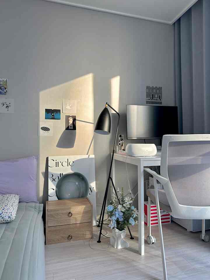 グレーの壁と木目調の床があるコンパクトなホームオフィス、白いデスクとオフィスチェア、フロアランプと収納家具が調和したシンプルモダンなインテリア