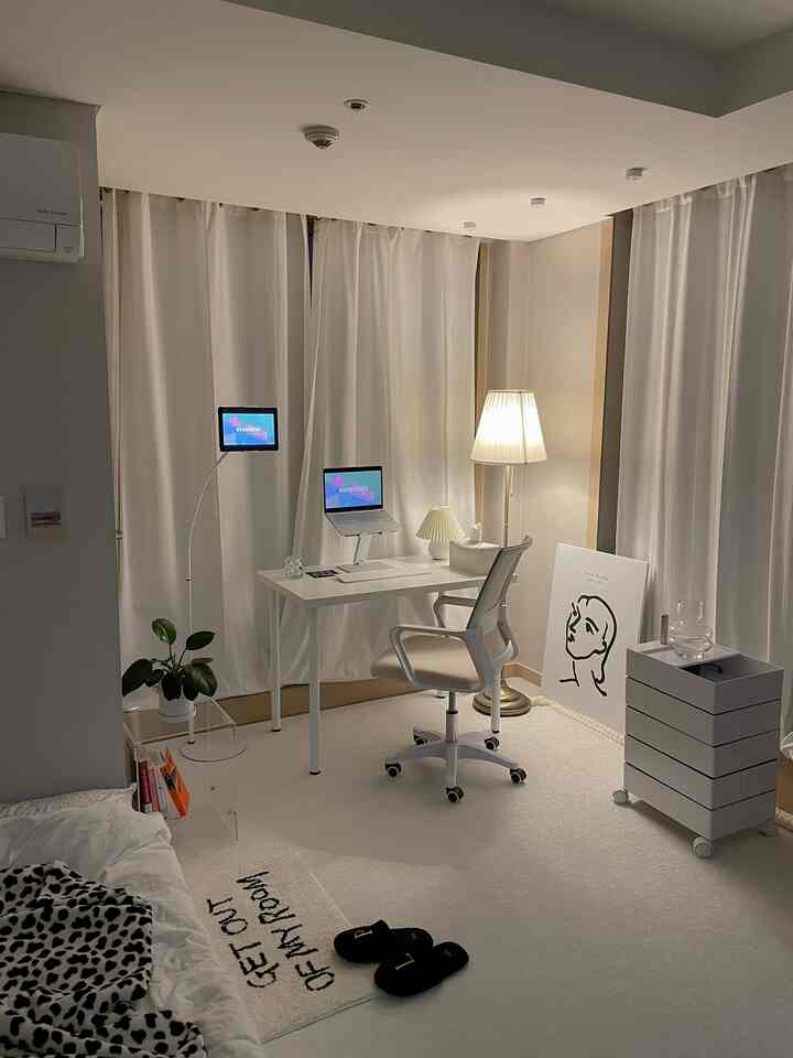 明るい白とベージュ調のワンルーム寝室のホームオフィス空間、イケアのデスクと快適なオフィスチェア、フロアランプとラグが調和した雰囲気のあるインテリア