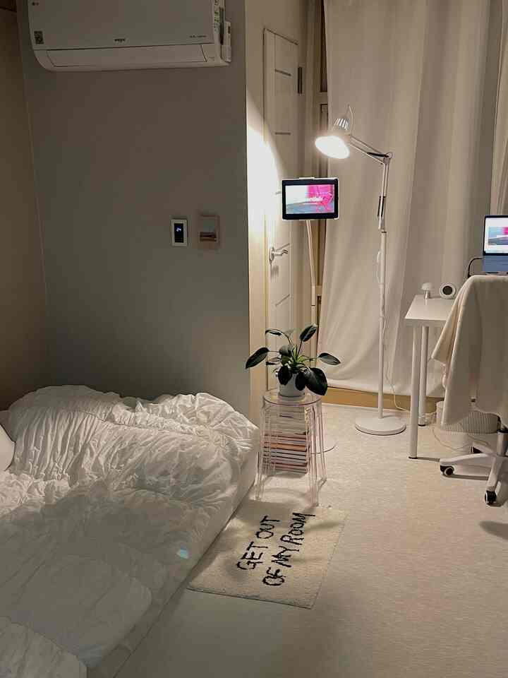 白色調の寝室、床に寝具があり、デスクとフロアランプが配置された雰囲気のあるインテリア