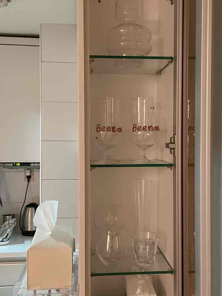 白を基調としたキッチン内の埋め込みガラス棚に様々なグラスと花瓶が整然と配置された雰囲気のあるインテリア